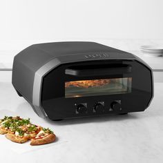 a pizza oven sitting on top of a counter next to a slice of pizza in front of it