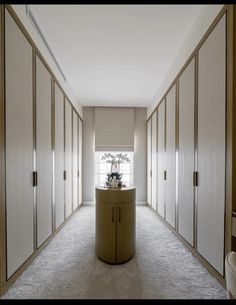 a long hallway with white walls and beige cupboards on both sides, leading to a window