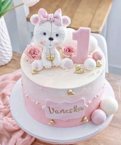 a pink and white cake with a teddy bear on top