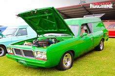 an old green car with its hood open in front of other older cars on display