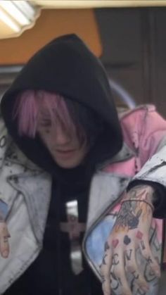 a man with pink hair and tattoos on his arm wearing a black hoodie jacket