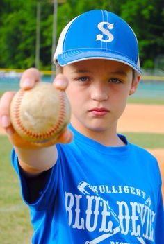 a young boy holding a baseball in his right hand and wearing a blue shirt with the s on it