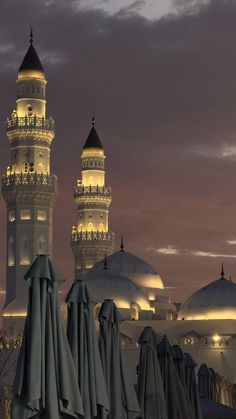 two tall white buildings sitting next to each other under a cloudy sky with umbrellas in the foreground