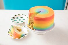 a rainbow colored cake sitting on top of a white table next to plates and bowls