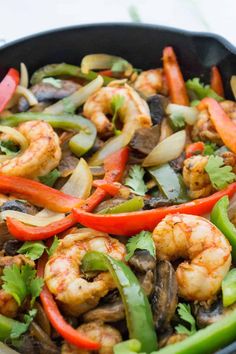 a skillet filled with shrimp, peppers and mushrooms on top of a white table