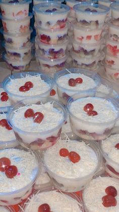 many desserts are arranged in plastic containers on the table with cherries and whipped cream