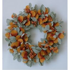 a wreath with orange flowers and green leaves on the front, sitting on a white surface