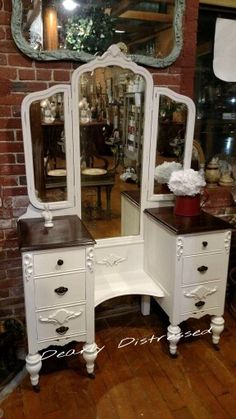 an antique vanity with mirror and stool in front of a brick wall, sitting on a hardwood floor