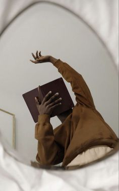 a woman reading a book in front of a round mirror with her hands on top of the book