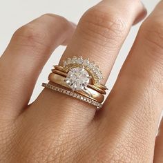 a woman's hand with two wedding rings on her fingers and the ring has an oval shaped diamond surrounded by smaller round diamonds