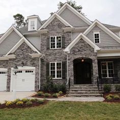 a large gray brick house with white trim on the front door and two story windows