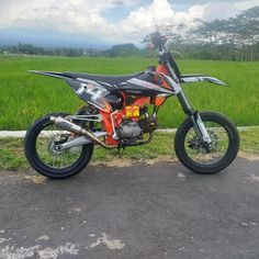 an orange and black dirt bike parked on the side of a road in front of some green grass