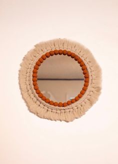 a round mirror hanging on the side of a wall with tassels around it