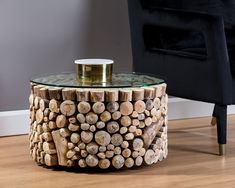 a table made out of logs with a glass top on the floor next to a chair