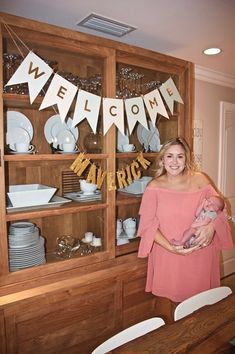 a woman standing in front of a wooden cabinet holding a baby