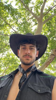 a man wearing a cowboy hat standing in front of a tree and looking at the camera