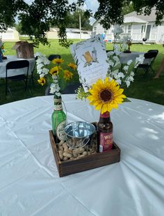 a wooden tray with bottles and flowers on top of a white table cloth covered table