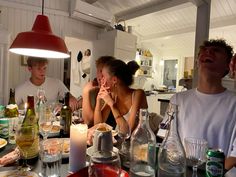 a group of people sitting around a table with bottles and glasses on it, all looking up