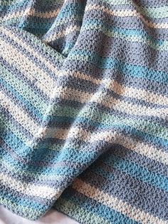 there is a crocheted blanket on top of a white bed sheet with blue and green stripes