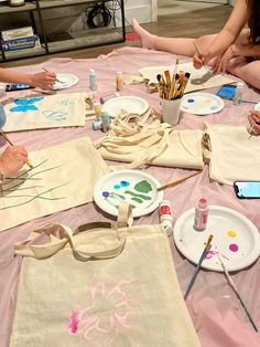 people sitting at a table with art supplies and paintbrushes on the tablescloth