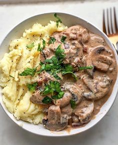 a white bowl filled with mashed potatoes and meat covered in mushroom gravy