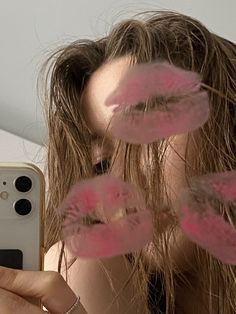 a woman taking a selfie with pink feathers on her hair while holding a cell phone