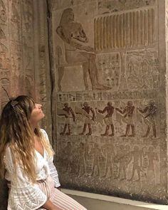 a woman sitting in front of a wall with egyptian paintings on it's side