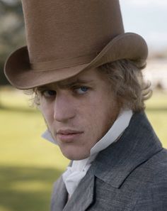 a man wearing a brown top hat with blue eyes and blonde hair in a park setting