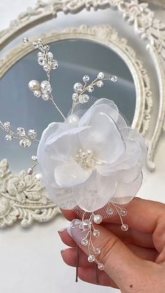 a hand holding a white flower on top of a hair comb in front of a mirror