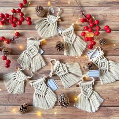 several tasselled ornaments with pine cones and berries on a wooden table next to christmas lights