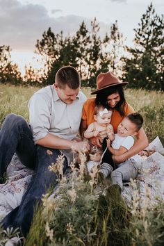 a man, woman and two children sitting on a blanket in the middle of a field