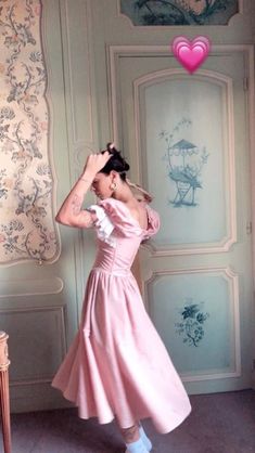 a woman in a pink dress is leaning against a wall with her hand on her head