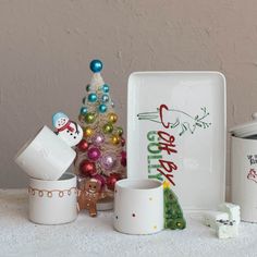 there are christmas decorations on the table next to cups and mugs, with a small tree in the background