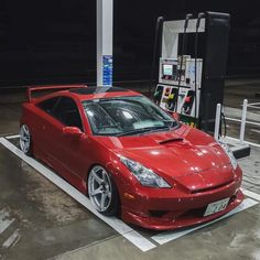 a red sports car is parked in a parking lot next to a gas station pump