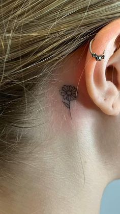 a woman's ear has a small flower tattoo on it