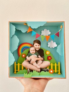 a person holding up a photo in a box with a rainbow and clouds on it