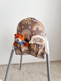 a teddy bear sitting in a high chair with a blanket on it's back