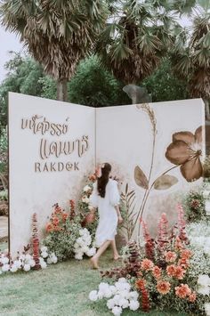 a woman walking past a sign with flowers on it in front of trees and bushes