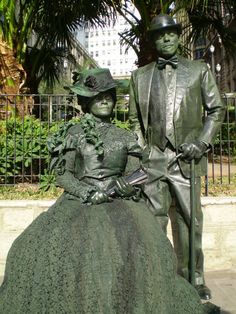 a statue of a man and woman sitting next to each other in front of a fence