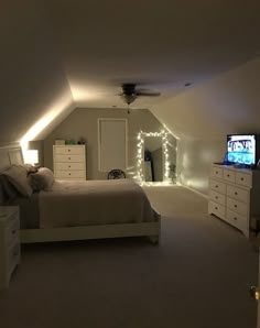 a bedroom with a bed, dressers and television in the corner is lit up by white lights