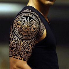 a man wearing a black shirt with gold tattoos on his arm and shoulder, standing in front of a mirror