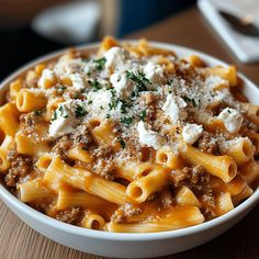 a white bowl filled with pasta covered in meat and cheese on top of a wooden table