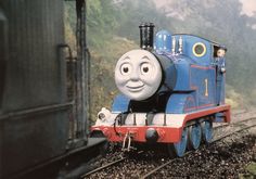 a thomas the tank engine is coming down the tracks with its eyes open and tongue out