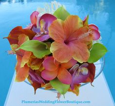 an arrangement of flowers in a glass vase on the edge of a swimming pool with blue water