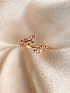 a gold ring with leaves on it sitting on top of a white satin material fabric