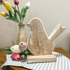 a small wooden bird sitting on top of a table next to some tulips