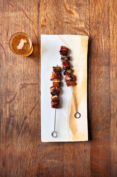 several skewered meats are sitting on a plate next to a glass of beer