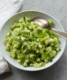 a white bowl filled with chopped cucumbers next to a silver spoon and napkin