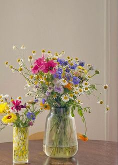 two vases filled with flowers sitting on top of a wooden table next to each other