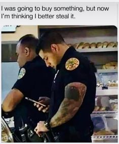 two police officers standing in front of a counter looking at their cell phones and texting to each other